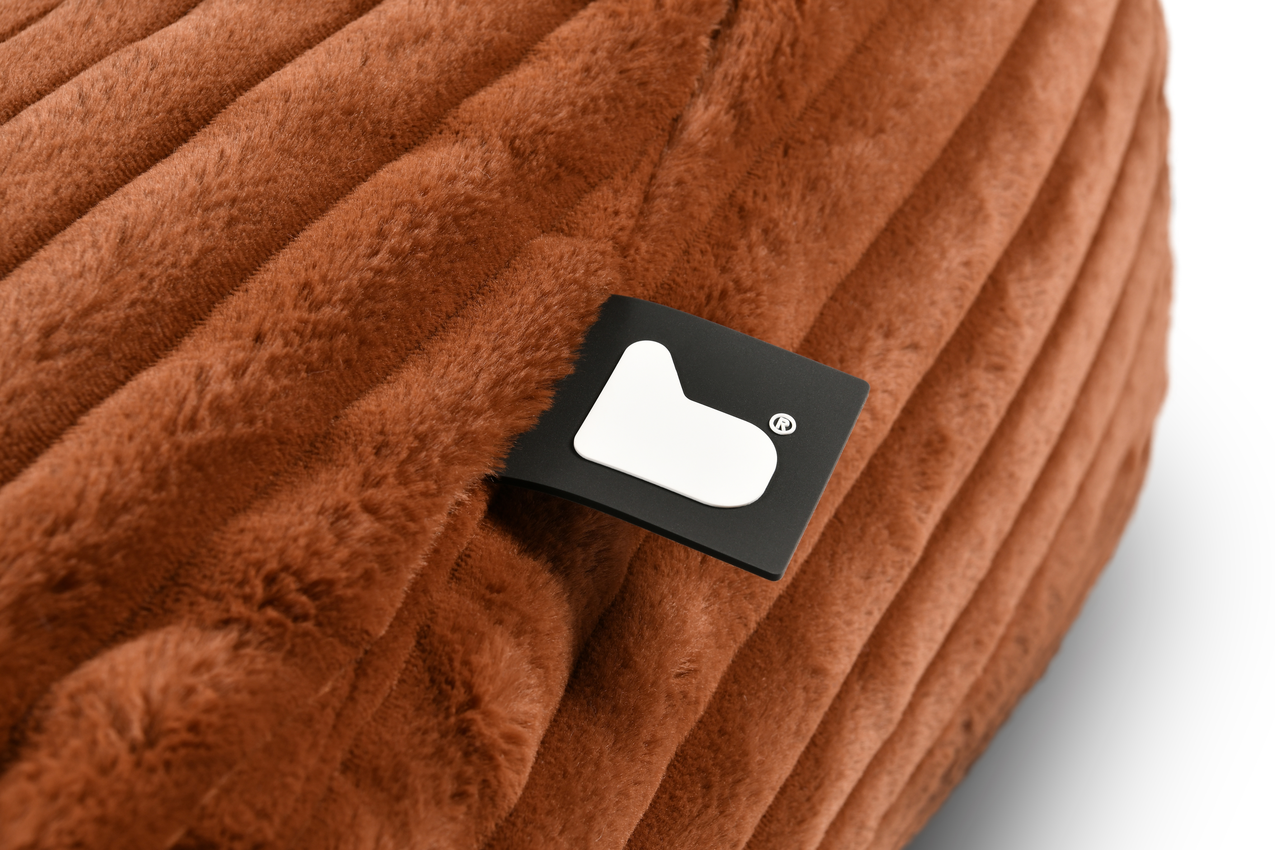 Close-up of a black clothing label on rust-coloured quilted fabric.